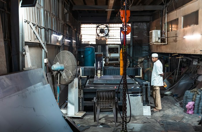 A man in white standing in a busy metal fabrication workshop in Mumbai